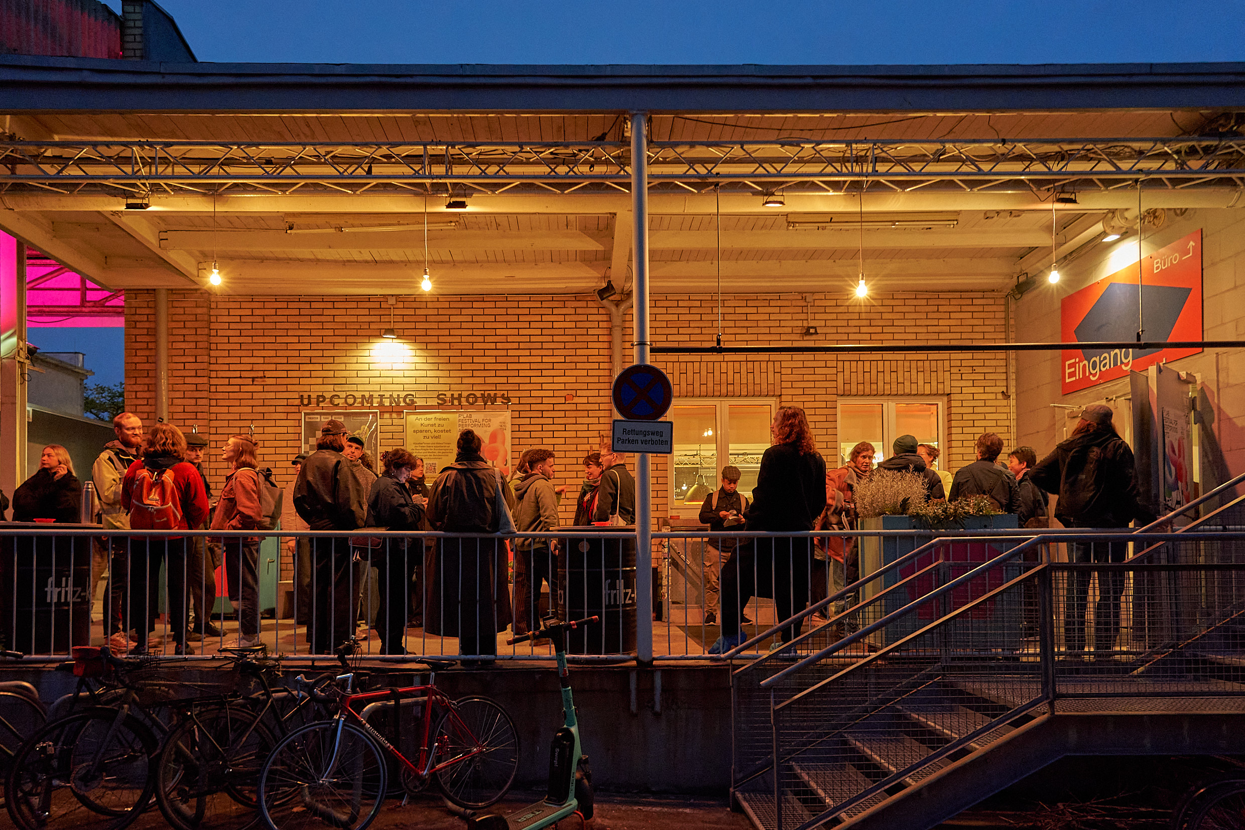 Viele Menschen stehen vor dem Eingangsbereich, beleuchtet von gelben Glühbirnen.
