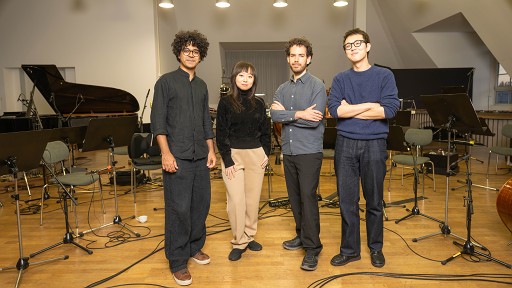 Vier junge Musiker*Innen umgeben von Notenständer und Instrumenten