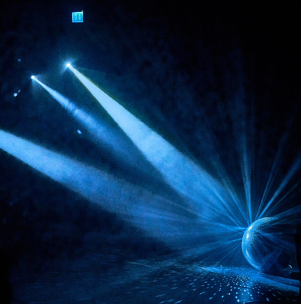 A disco ball lying on the floor is hit by several blueish light beams.