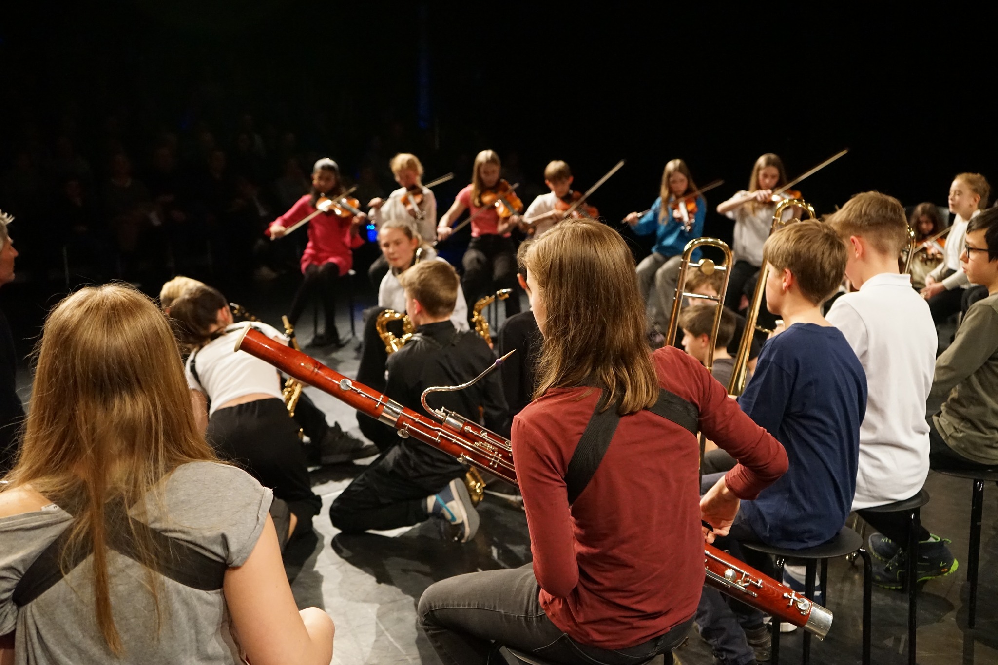 A class of seventh graders sitting in half circle. There are two rows. Each kid holds an instrument.  