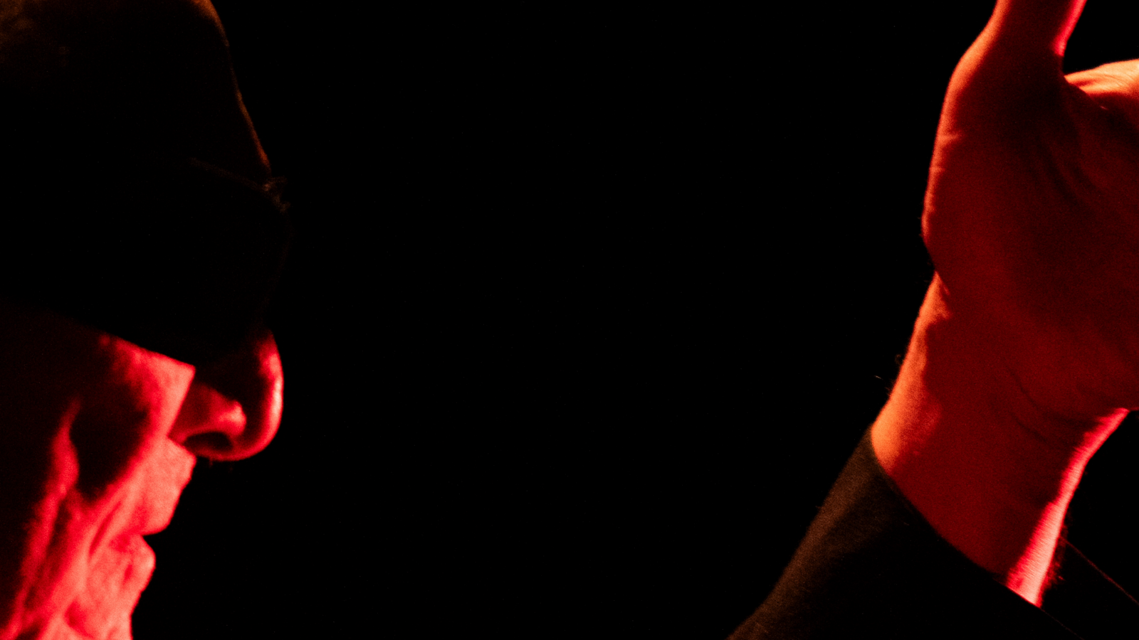The section of the photo shows a person's hand and shaded parts of their face against a dark background.