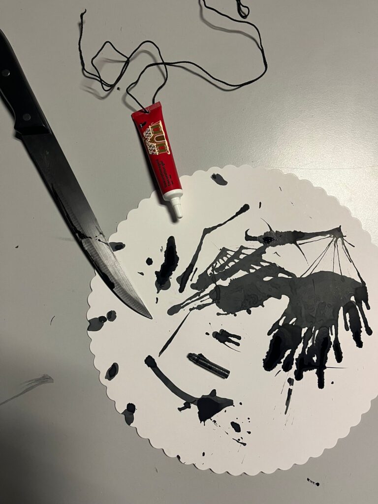 Ein scharfes Messer und eine Farbtube auf einem Pappteller . Der Pappteller ist mit schwarzer Farbe verschmiert. 