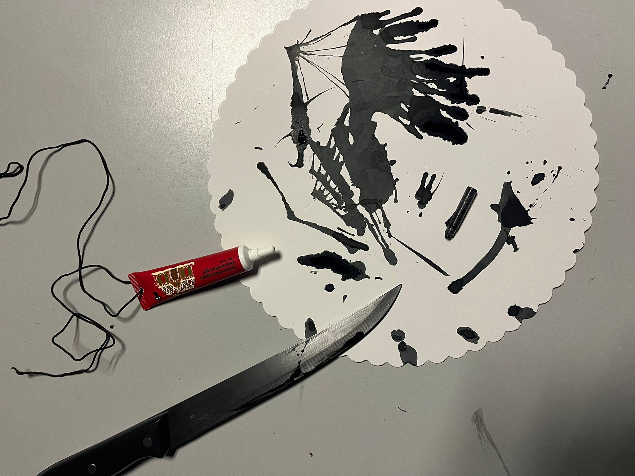 A sharp knife and a tube of paint on a paper plate. The paper plate is smeared with black paint. 