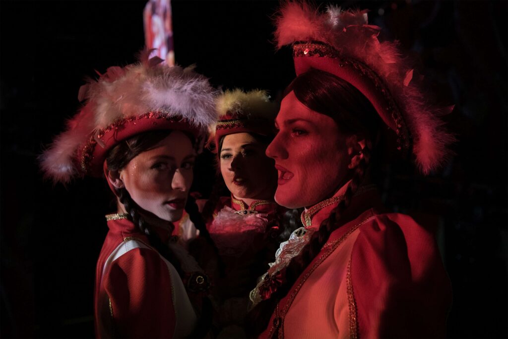 Die Gesichter von drei Frauen mit Karnevalshüten und Uniformen.