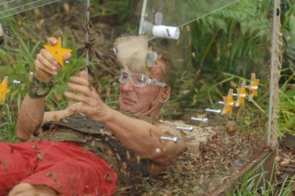 Ein Man in kurzen roten Hosen und mit einer Schwimmbrille liegt in einem Glaskasten, der in der Natur steht.