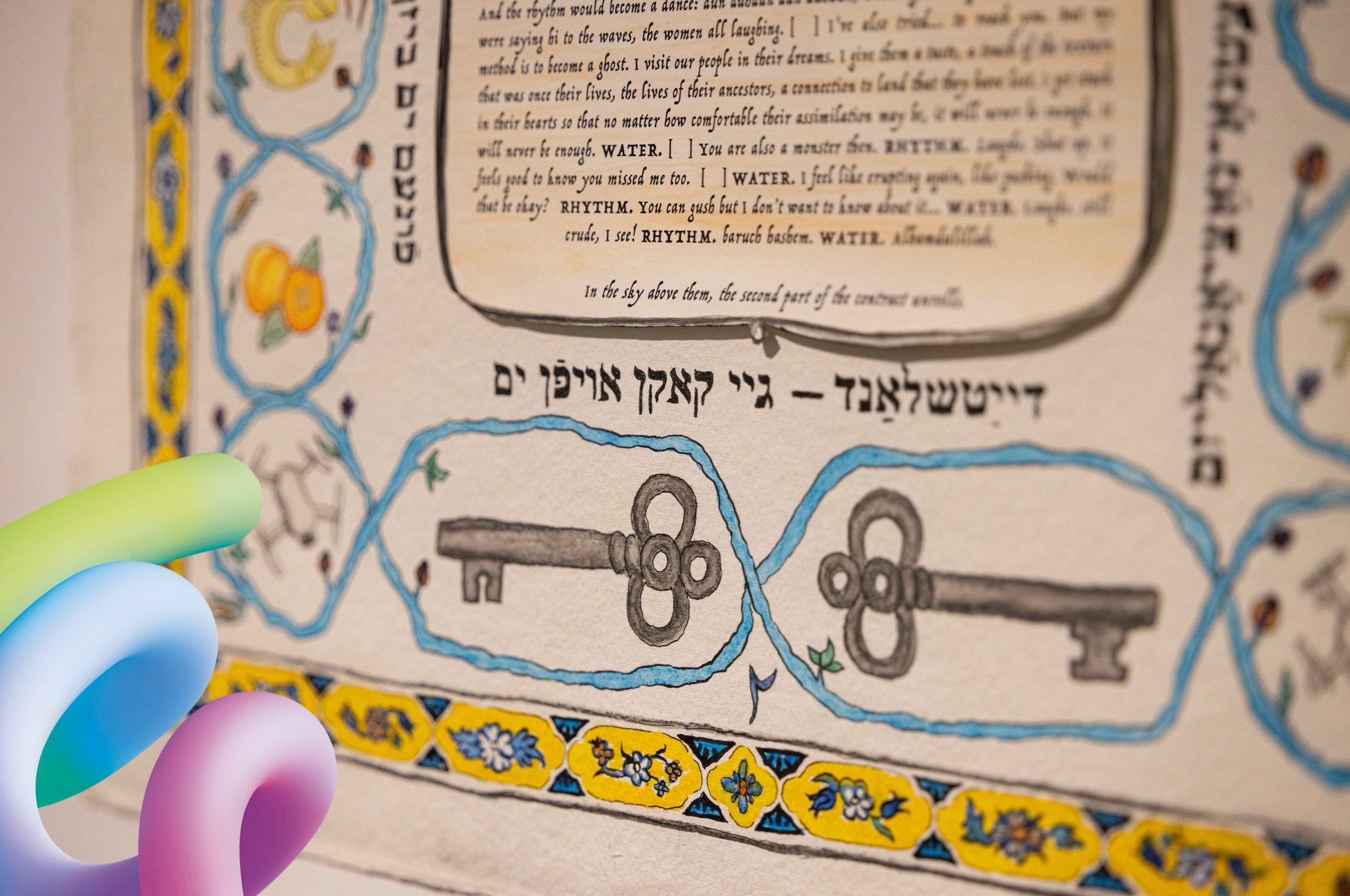 Das Foto zeigt einen Ausschnitt eines Posters, auf dem hebräischer und englischer Text abgedruckt sind, umgeben von einer gezeichneten Bordüre in blau und geld mit Blumen und zwei großen, antiken Schlüsseln.