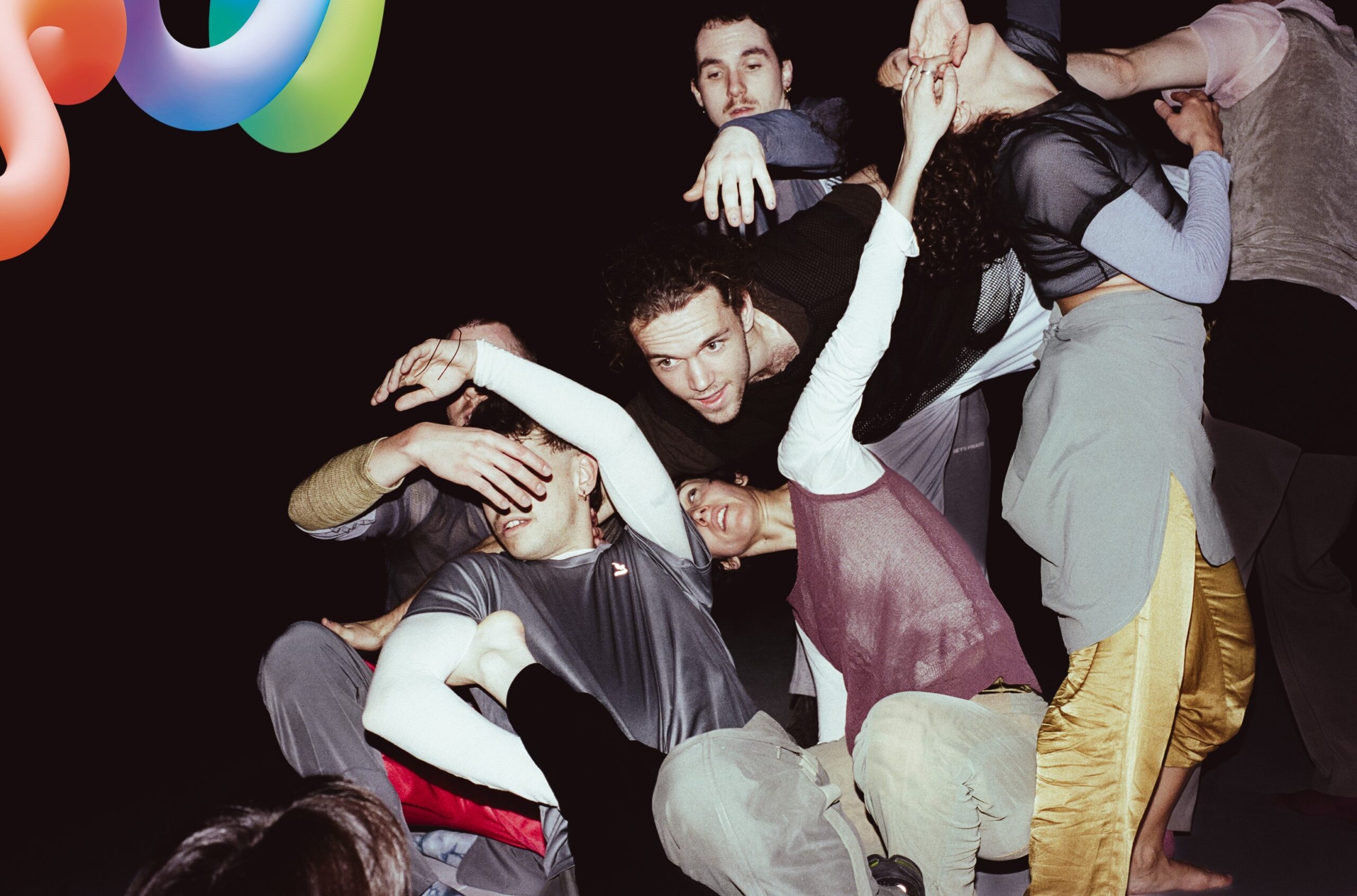 Das Bild zeigt einen Haufen Menschen vor schwarzem Hintergrund, die in engem Kontakt zueinander sind und sich wie eine Kaskade von rechts oben nach links unten bewegen.
