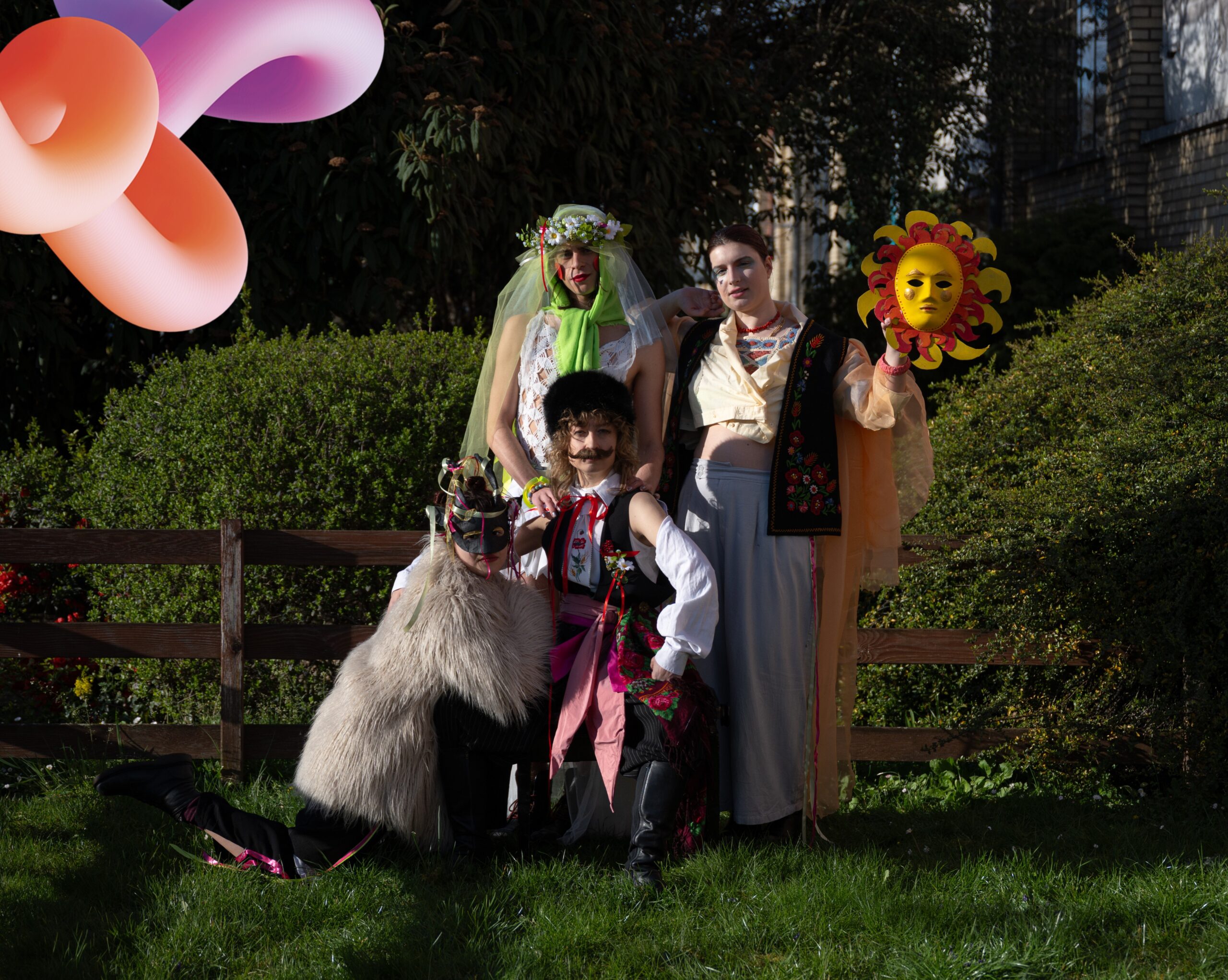 Das Bild zeigt eine Gruppe von vier Performer*innen in einem Garten, die aufwändig kostümiert sind. Eine Person ist als Mann verkleidet, eine weitere als Braut, eine dritte trägt Fellmantel und Tiermaske und die vierte Person hält neben den Kopf die Maske einer Sonne.