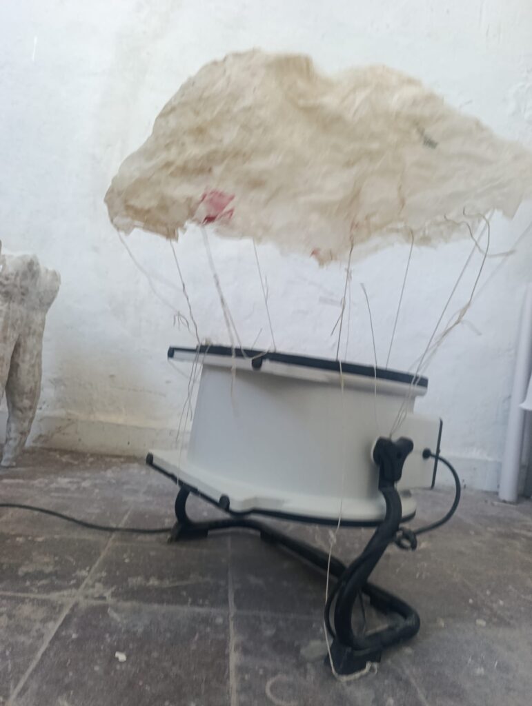 Ein großer Ventilator pustet ein weißes Tuch an Fäden hoch.